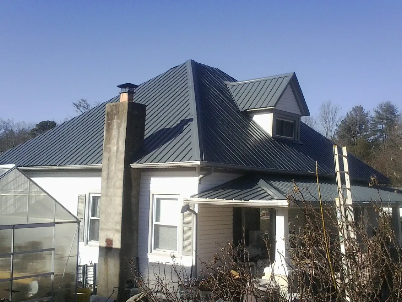 Dark blue standing seam metal roof on a white farmhouse with dormer — Slate & Tile Roof Repair by Roofing Brothers in Schaefferstown