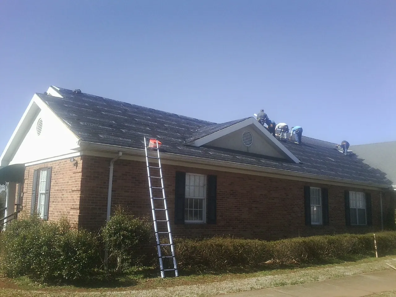 Crew tearing shingles off a brick ranch roof with a ladder set — Metal Roof Repair work by our crew in Schaefferstown
