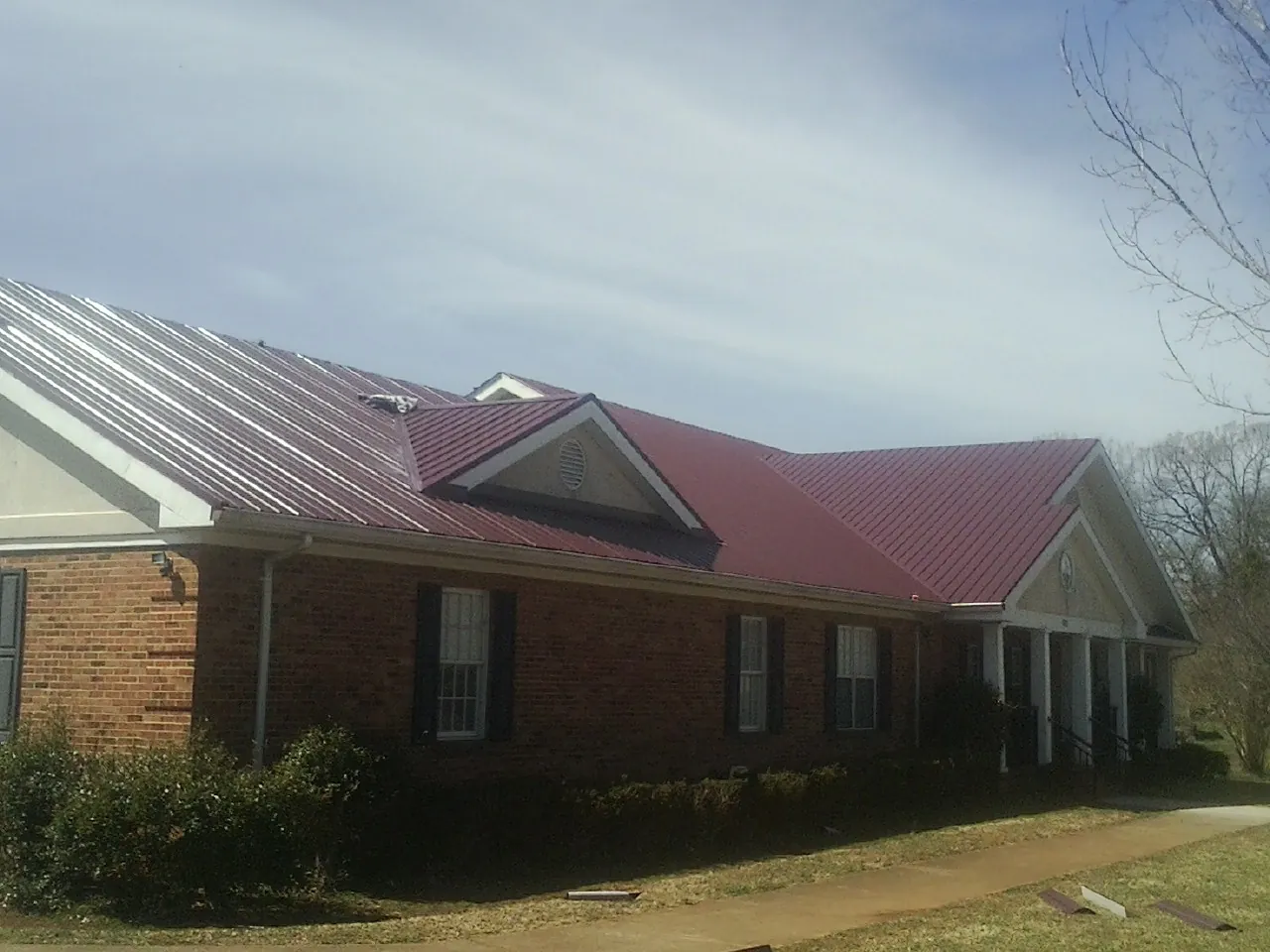 Red metal roof with gabled entries on a long brick building, from a Hail Damage Roof Repair job in Schaefferstown