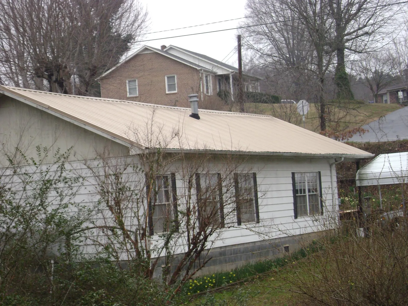 Tan metal roof on a white sided house set into a hillside — Commercial Roofing by Roofing Brothers in Schaefferstown